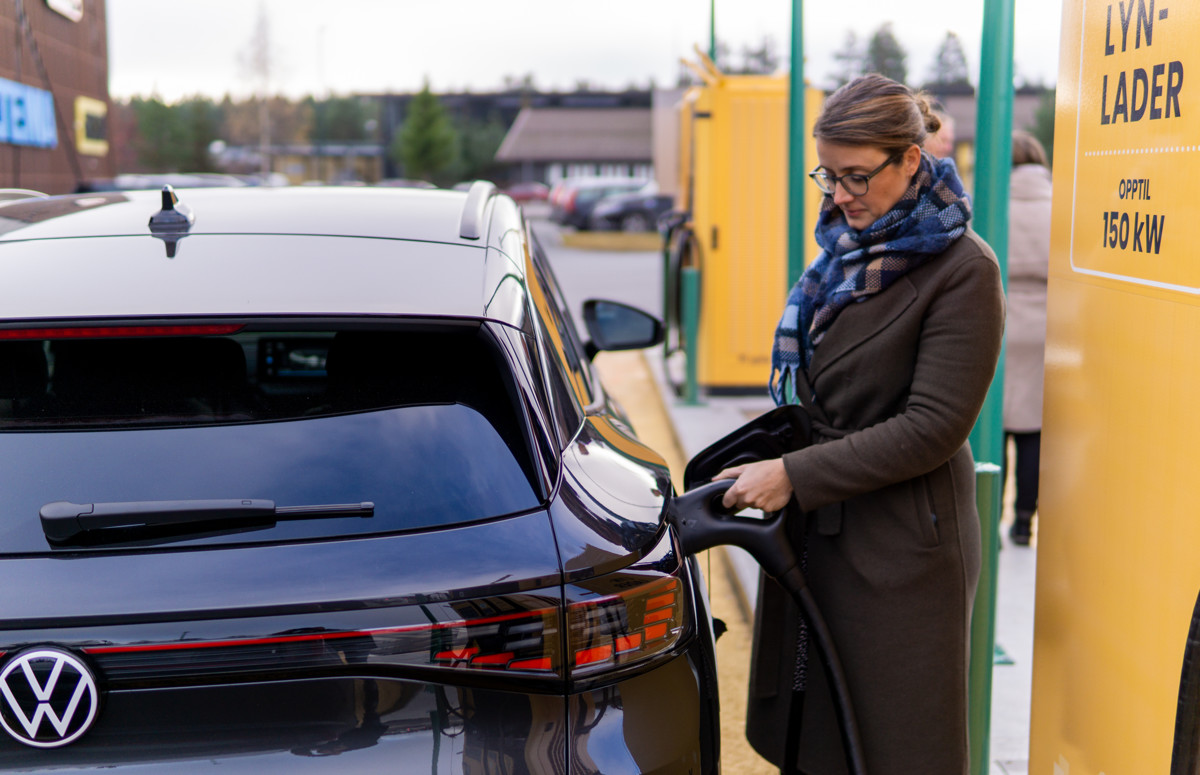 vinne i vinterkl&aelig;r lader en svart Volkswagen elbil ved en gul lynladestasjon